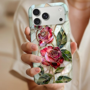 Puede incluir: Funda de teléfono inteligente con un diseño de vidriera que presenta dos rosas rojas, hojas verdes y contornos dorados. La funda tiene un fondo claro con un patrón de mosaico y un módulo de cámara.