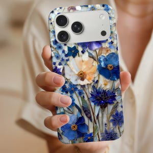 Peut inclure: Coque de téléphone à motif floral en mosaïque. Elle présente des fleurs bleues, blanches et orange avec des pétales détaillés et des centres dorés. La coque a une finition brillante et une découpe pour l'appareil photo.
