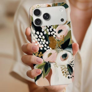 May include: A floral phone case featuring a colorful abstract design. The case has a white background with pink, green, gold, and black brushstrokes. The case has a camera cutout and is held in a person's hand.