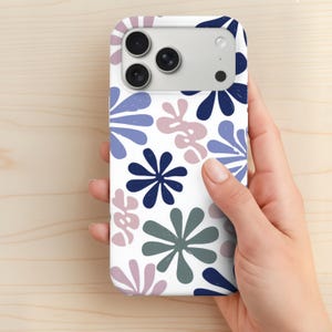 May include: A white phone case featuring a floral pattern in shades of blue, gray, and pink. The case has a protective bumper and cutouts for the camera and buttons. The design is a repeating pattern of stylized flowers.