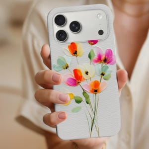 May include: A light gray phone case featuring a colorful floral design. The flowers are painted in shades of orange, pink, yellow, and blue, with green stems. The case has a textured surface and a camera module with multiple lenses.