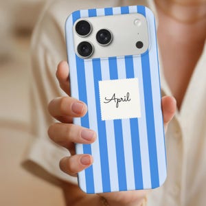 May include: A blue and white striped phone case with the word "April" on a white square. The case has a camera module with three lenses and a flash.