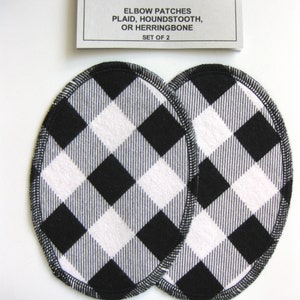 May include: Two black and white plaid elbow patches, each with a black stitched edge. The patches are oval shaped and are sold as a set of two. The text on the label reads "CRAFT ♥ T'S ELBOW PATCHES PLAID, HOUNDSTOOTH, OR HERRINGBONE SET OF 2".