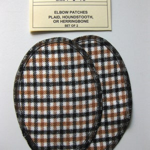 Puede incluir: Dos parches para codos de cuadros marrones y negros con costuras negras. Los parches son de forma ovalada y están etiquetados como "CRAFT ♥ T'S ELBOW PATCHES PLAID, HOUNDSTOOTH, OR HERRINGBONE SET OF 2".