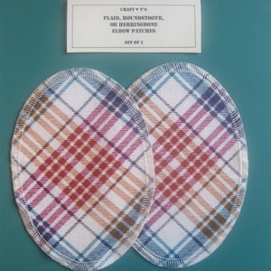May include: Set of two plaid elbow patches for clothing repair. The patches are oval shaped and feature a white background with a red, blue, and brown plaid pattern. The patches are edged with a blue and white zig-zag stitch. The text on the label reads "CRAFT ♥ T'S PLAID, HOUNDSTOOTH, OR HERRINGBONE ELBOW PATCHES SET OF 2".