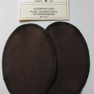 May include: Two brown elbow patches with black edging. The patches are made of a herringbone fabric. The text on the label reads "CRAFT ♥ T'S ELBOW PATCHES PLAID, HOUNDSTOOTH, OR HERRINGBONE SET OF 2".