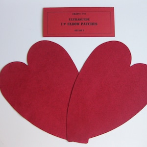 May include: Two red heart-shaped elbow patches made of ultrasuede fabric. The patches are packaged in a red card with the text "Craft + T's Ultrasuede I ♥ Elbow Patches Set of 2".
