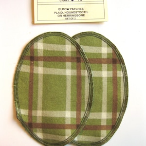 Pode incluir: Dois remendos para cotovelos em tecido xadrez verde, marrom e branco com uma costura em ziguezague ao redor das bordas. Os remendos são de forma oval e são etiquetados como "CRAFT ♥ T'S ELBOW PATCHES PLAID, HOUNDSTOOTH, OR HERRINGBONE SET OF 2".