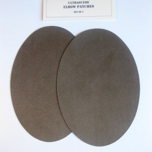 May include: Two brown ultrasuede elbow patches, set of 2.  The patches are round and have a textured surface.