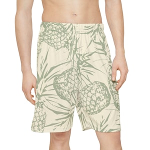May include: Cream-coloured shorts featuring a repeating pattern of green pineapples and leaves. The shorts have an elasticated waistband and are knee-length, suitable for casual wear or beach outings.