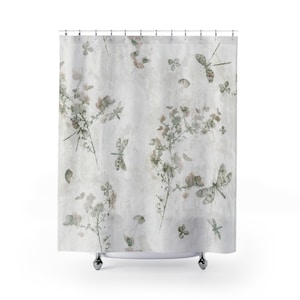 May include: A shower curtain with a botanical design. The curtain features a light gray background with a pattern of dragonflies, flowers, and leaves in shades of green and beige. The curtain is hanging from a metal rod.