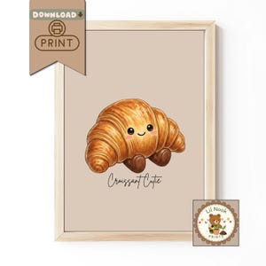 May include: A framed print of a cartoon croissant with a smiling face and small brown feet. The words "Croissant Cutie" are written below the pastry. The print is in a light brown frame, with a "Download Print" graphic in the upper left corner.
