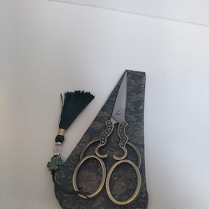 Peut inclure: Ciseaux décoratifs aux manches ornés et aux lames tranchantes, présentés dans un étui à motifs floraux vert foncé. Une pampille assortie avec un accent doré et un charme vert est suspendue à l'étui. Idéal pour le bricolage ou la couture.