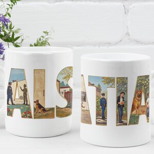 Puede incluir: Dos tazas de cerámica blanca con la palabra "ALSATIA" impresa. Las letras están llenas de ilustraciones de estilo vintage de personas, edificios y un perro pastor alemán. Las tazas están sobre un fondo de ladrillo blanco.