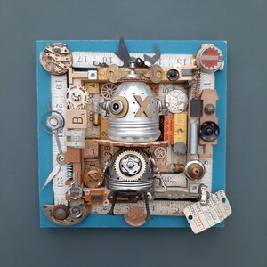 May include: A robot made of various metal and wood pieces, including rulers, gears, and a metal can. The robot is painted silver and has a black eye. The robot is on a blue background with a price tag that says "STOCK 3373".