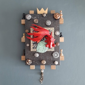 May include: A mixed media wall art piece featuring a red betta fish, a gold crown, and various buttons and other embellishments on a black background.