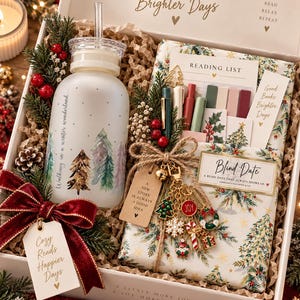 May include: A gift box containing a frosted glass bottle with a winter tree print, a wrapped book labeled Blind Date, a reading list card, colorful sticky tabs, pens, and a gold-toned charm keychain with holiday icons, all nestled in paper filler.