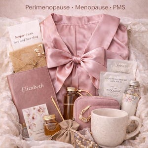 May include: A pink Women's Transition Care Kit with a robe, journal, and various self-care items. The kit includes a mug, small bottles, a pouch, and a small bag of beads. The text on the box reads "Support for Every Season of Her Body."