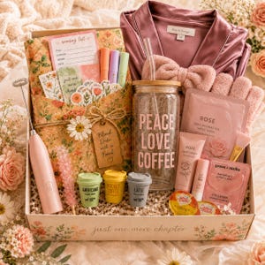 May include: A gift box containing a floral-patterned book sleeve, a pink satin robe, a glass tumbler with a straw and the text PEACE LOVE COFFEE, a handheld milk frother, rose-scented skincare products, collagen eye masks, and miniature coffee cups.