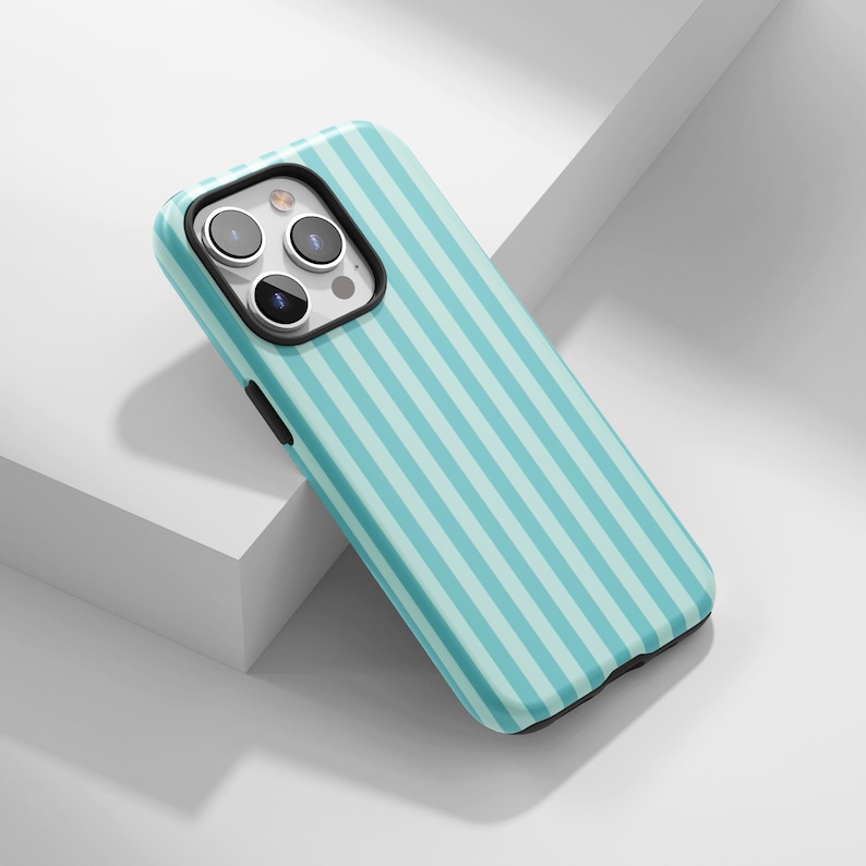 May include: A teal and light blue striped phone case. The case has a black border around the camera and a black button on the side. The case is designed to fit a smartphone.