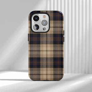 May include: A smartphone case featuring a classic plaid pattern in shades of tan, dark navy blue, and thin brown intersecting lines. The case has a rectangular shape with rounded corners and a cutout for a triple-lens camera system on the back.