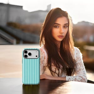 May include: A teal and white striped phone case. The case has a vertical stripe pattern and a camera cutout. The phone case is on a dark surface.