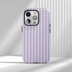 May include: A smartphone case featuring a vertical striped pattern in alternating shades of light lavender and white. The case has a black camera module cutout on the back, revealing three circular camera lenses and a flash component.