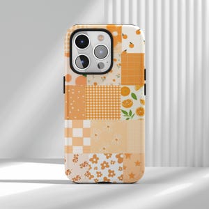May include: A phone case with a patchwork design in shades of orange and white. The case features various patterns, including gingham, floral, and polka dots, with orange fruit illustrations. The case has a black border and a camera cutout.