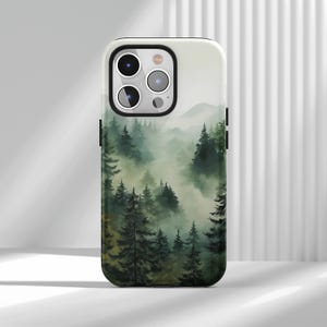 May include: A phone case with a watercolour painting of a misty forest scene. The design shows layers of green trees and soft, atmospheric fog, with subtle mountain silhouettes in the background. The case has a glossy finish and black side accents.