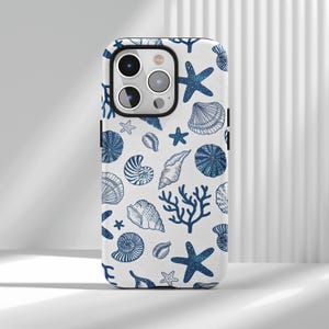 May include: A white phone case with a blue nautical pattern. The design features seashells, starfish, and coral. The case has a glossy finish and a camera cutout.