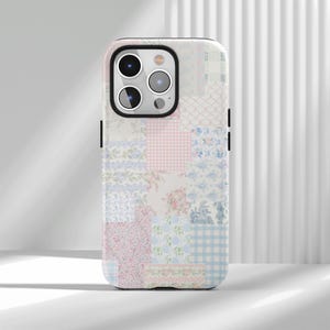 Könnte beinhalten: Eine Smartphone-Hülle mit einem Patchwork-Design aus verschiedenen Blumen-, Vichy- und Toile-Mustern in zarten Rosa-, Hellblau- und Weißtönen. Die Hülle hat eine rechteckige Form mit abgerundeten Ecken und einen Ausschnitt für eine Dreifachkamera.