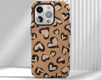 May include: A phone case with a brown and tan heart-shaped leopard print design. The case has a black border around the camera and a black side button. The background is a white wall with vertical lines.