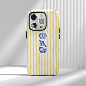 Op de afbeelding: Een telefoonhoesje met een geel en wit gestreept patroon. De hoes heeft drie blauwe illustraties van zeeschelpen. De telefoonhoes heeft een zwarte rand rond de camera en zijkanten.