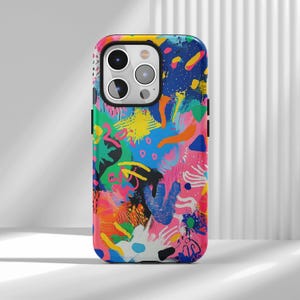 Könnte beinhalten: Eine Smartphone-Hülle mit einem lebendigen, mehrfarbigen abstrakten Muster mit Spritzern in Blau, Pink, Gelb, Grün, Orange und Schwarz. Das Design umfasst verschiedene Pinselstriche, Punkte und organische Formen auf der gesamten Oberfläche.