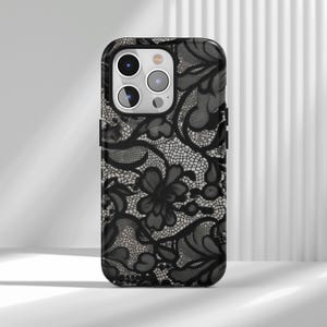 May include: Black phone case with a detailed lace pattern. The case features a floral design with intricate details and a glossy finish. The case has a camera cutout and button covers.