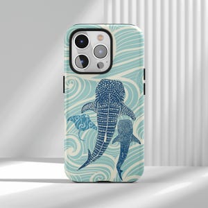 May include: A phone case featuring a blue and white ocean-themed design with illustrations of a whale shark, a manta ray, and a smaller shark. The case has a glossy finish and a black border.