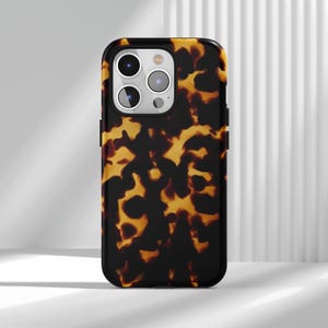 Pode incluir: Capa de telemóvel com padrão de tartaruga em preto e castanho. A capa tem um acabamento brilhante e uma borda preta. As lentes da câmara são visíveis na parte superior. A capa foi concebida para um smartphone.