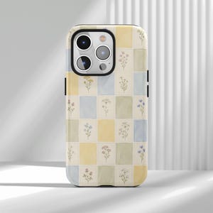 May include: A smartphone case featuring a grid pattern of alternating pastel yellow, light blue, and sage green rectangular blocks. Each block contains a small, delicate watercolor-style illustration of a different wildflower or botanical sprig.