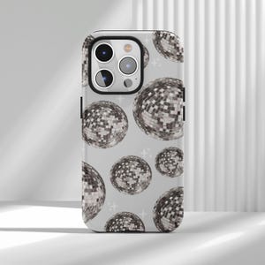 Könnte beinhalten: Handyhülle mit einem Muster aus silbernen Discokugeln auf hellgrauem Hintergrund. Die Hülle hat einen schwarzen Rand und einen Kameraausschnitt. Die Discokugeln sind unterschiedlich groß und über die Oberfläche verteilt.