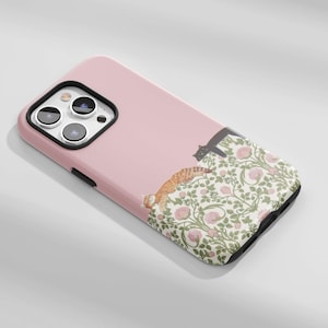May include: A pink phone case featuring a floral pattern with pink roses and green leaves. Two cats are depicted on the case, one orange tabby and one black cat. The case has a camera cutout and black trim.