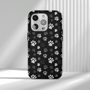 May include: Black phone case with a repeating pattern of white and gray paw prints. The case has a glossy finish and a camera cutout. The design is a playful and pet-friendly accessory.