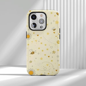 Könnte beinhalten: Hellgelbe Handyhülle mit einem sich wiederholenden Muster aus Bienen, Sternen, Herzen und Blumen. Die Hülle hat einen schwarzen Rand und einen Kameraausschnitt. Das Design ist skurril und fröhlich.