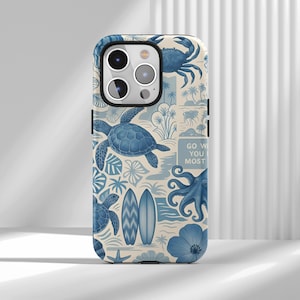 May include: A blue and white phone case featuring a coastal design. The case has illustrations of sea turtles, surfboards, an octopus, and a crab. The text "GO WITH YOU MOST" is also visible on the case.