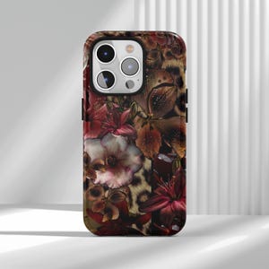 Könnte beinhalten: Eine Handyhülle mit einem Blumendesign aus roten, braunen und weißen Blumen. Der Hintergrund ist ein Leopardenmuster. Die Hülle hat eine glänzende Oberfläche und ist für ein Smartphone konzipiert.