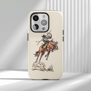 Peut inclure: Une coque de smartphone couleur crème ornée d'une illustration détaillée d'un cow-boy montant un cheval brun en plein rodéo. Le cavalier porte un chapeau et tient un lasso au-dessus de sa tête. Le motif inclut des nuages de poussière.