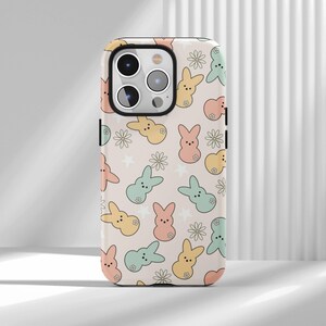 May include: A phone case with a repeating pattern of pastel-colored bunny and flower illustrations on a light beige background. The bunnies are in shades of pink, yellow, and blue, with small flower accents.