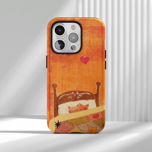 May include: A smartphone case featuring an orange background with a brown bed frame. Two cats are sleeping under a patchwork quilt decorated with a star and heart patterns. Two red hearts are floating above the bed in the upper section.