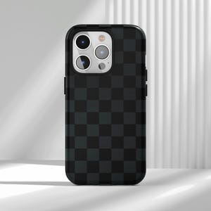 Pode incluir: Capa de telefone xadrez preta e cinza. A capa tem um padrão de grade de quadrados cinza escuro em um fundo preto. A capa do telefone tem um recorte para a câmera e botões.