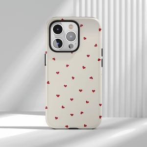 May include: A cream-coloured phone case featuring a pattern of small red hearts. The case has a black border and camera housing. The phone case is designed to fit a smartphone.