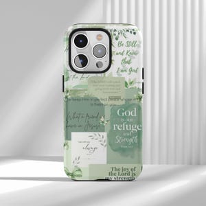 Puede incluir: Una funda de teléfono blanca y verde con citas inspiradoras y detalles florales. La funda presenta frases como "Be Still and Know that I am God" y "God is our refuge and strength". El diseño incluye un efecto de acuarela y elementos botánicos.